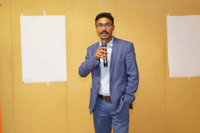 Adarshh Panndey speaking with a microphone in a meeting hall